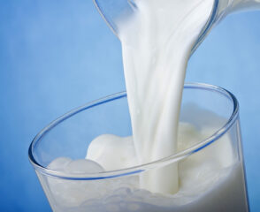 Pouring milk into a glass, blue background.
