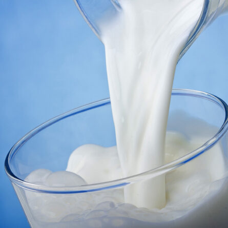 Pouring milk into a glass, blue background.