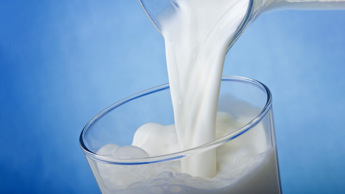 Pouring milk into a glass, blue background.