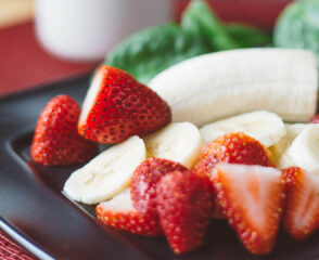 Strawberries and bananas on black plate.