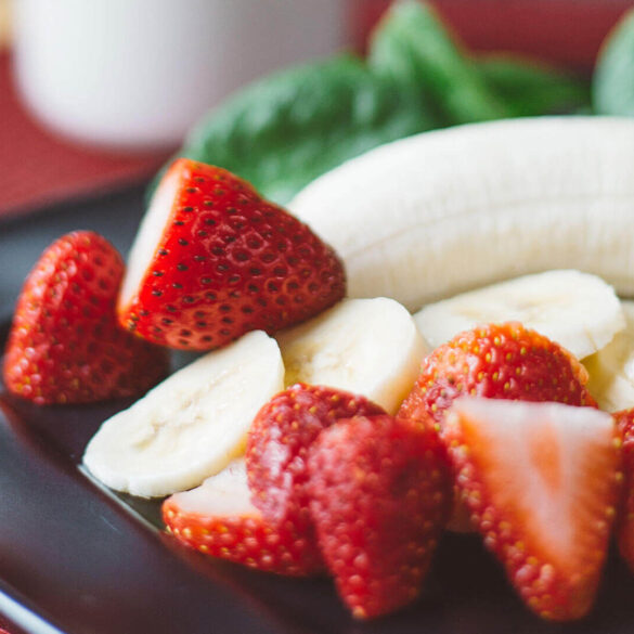 Strawberries and bananas on black plate.