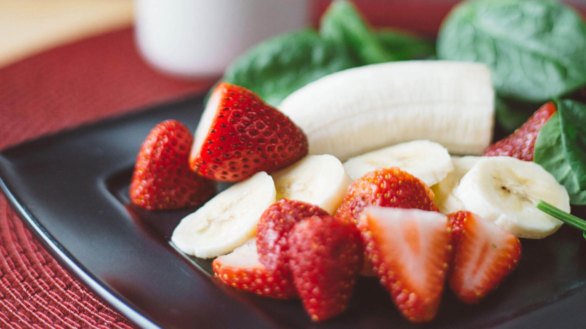 Strawberries and bananas on black plate.