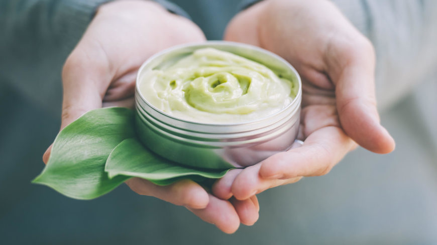 Hands holding green cream and leaf.