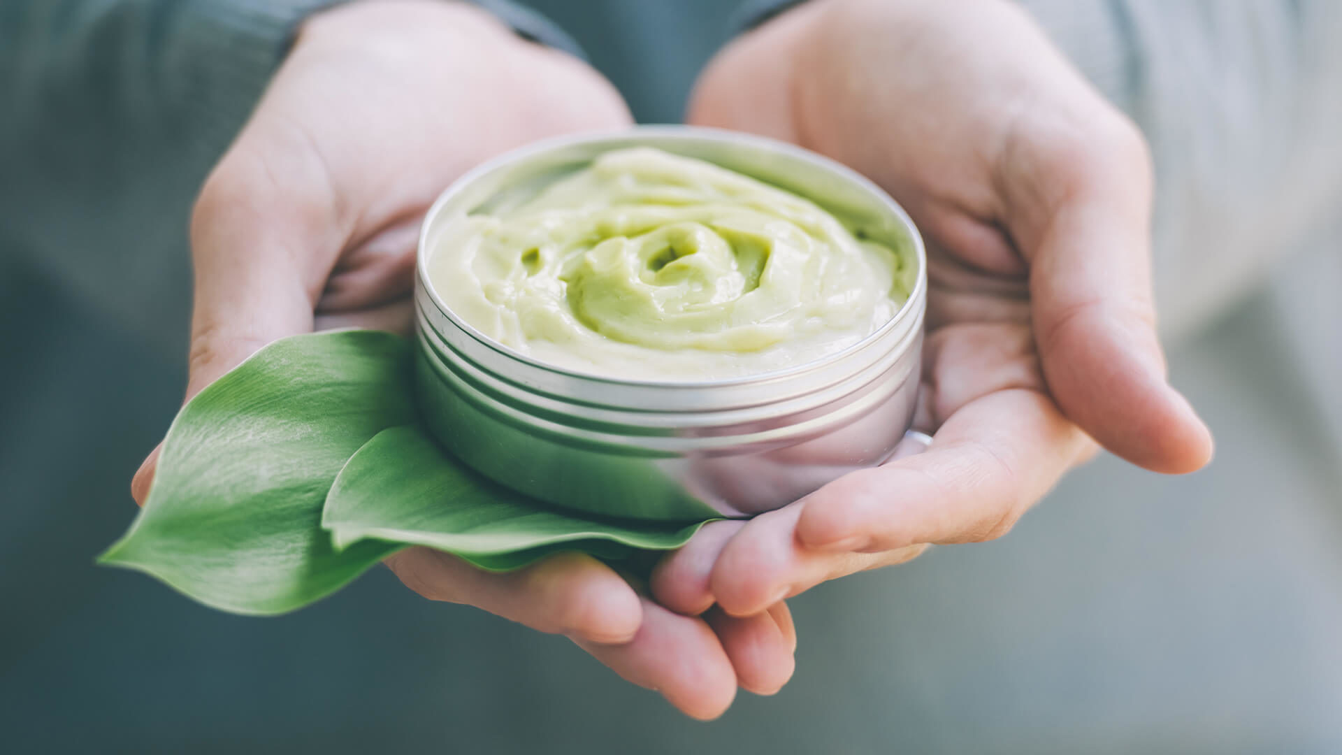 Hands holding green cream and leaf.