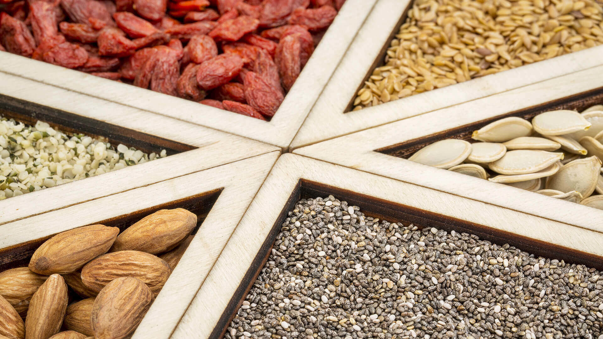 Assorted seeds and nuts in wooden sections.