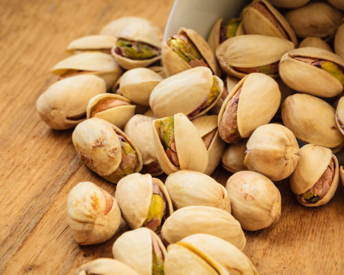 Pistachios scattered on wooden surface.