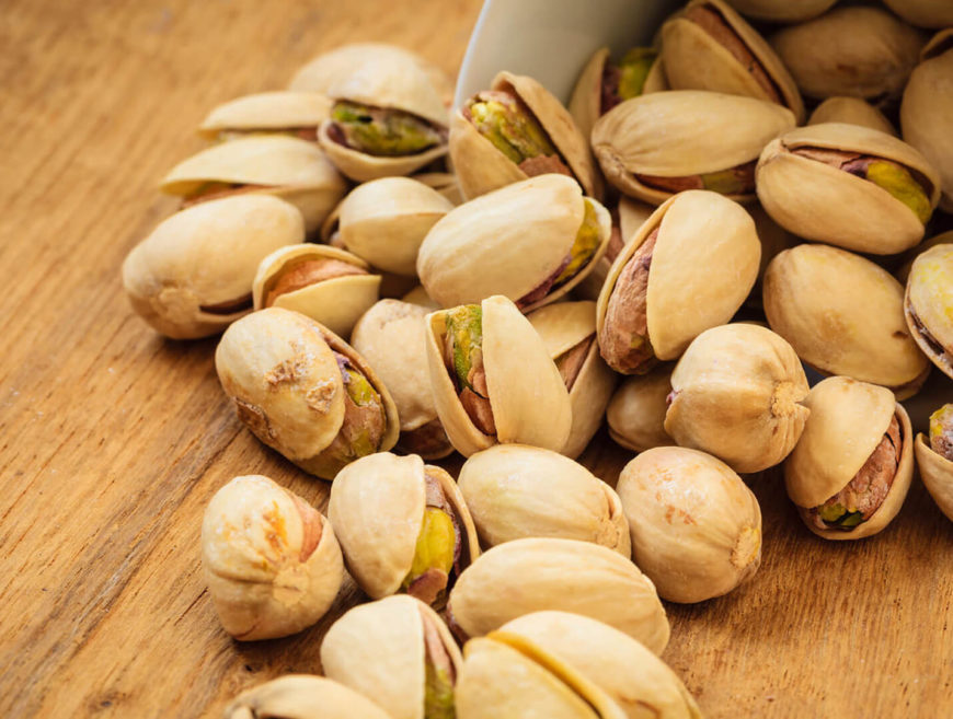 Pistachios scattered on wooden surface.