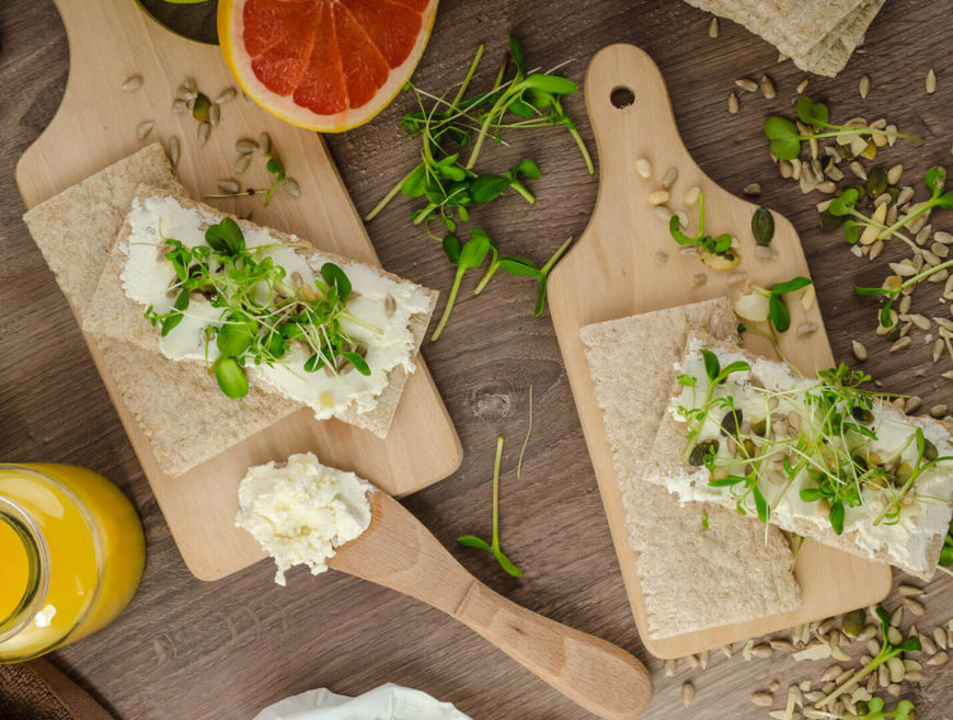 Crackers with cheese and sprouts on boards.
